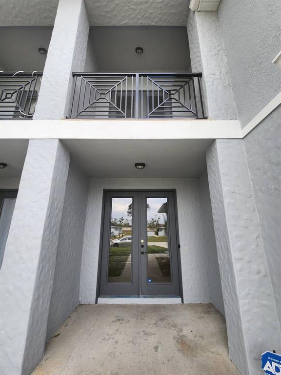 A ground-level entryway features double glass doors beneath a second-story balcony with metal railings — 328 DUNDEE DRIVE, KISSIMMEE, FL
