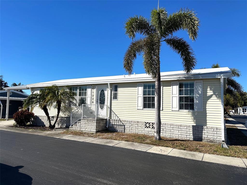 A light yellow manufactured home with a palm tree and a brick-patterned foundation — 11228 102ND STREET N UNIT 180, LARGO, FL