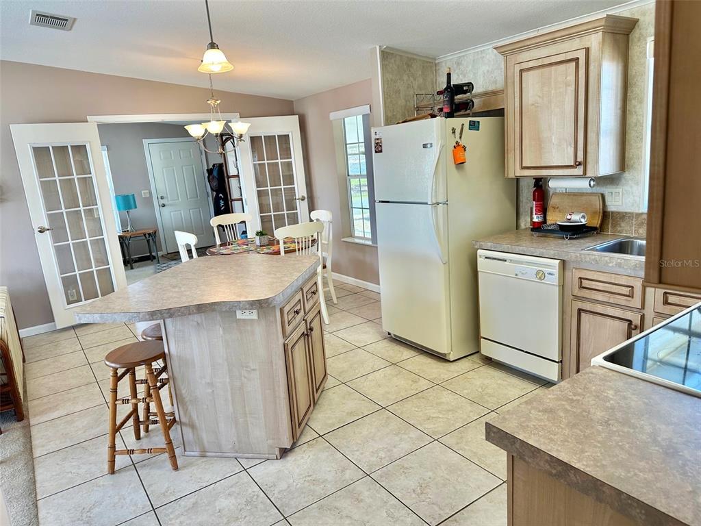 A kitchen features light wood cabinets, a central island with stools, and tile flooring — 11228 102ND STREET N UNIT 180, LARGO, FL
