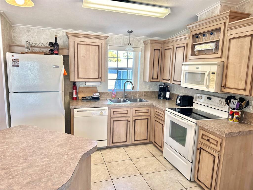 A kitchen features light wood cabinets, white appliances, a double sink, and tiled flooring — 11228 102ND STREET N UNIT 180, LARGO, FL