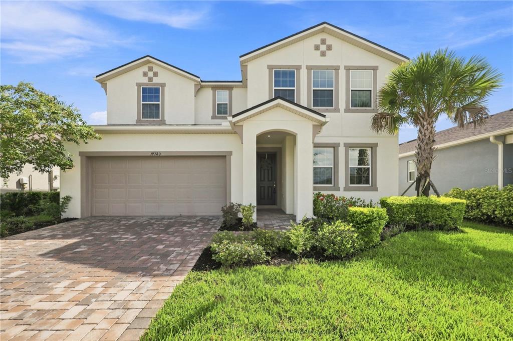 A two-story suburban house with a beige stucco exterior, a two-car garage, and a palm tree — 19780 BLUE POND DRIVE, LUTZ, FL
