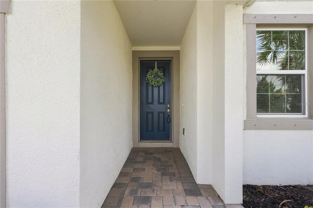 A dark blue front door with a wreath sits at the end of a paved entryway — 19780 BLUE POND DRIVE, LUTZ, FL