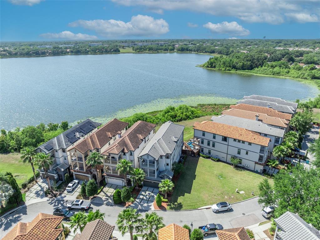 An aerial view shows several multi-story townhouses with tiled roofs situated beside a large lake — 7613 TOSCANA BOULEVARD, ORLANDO, FL