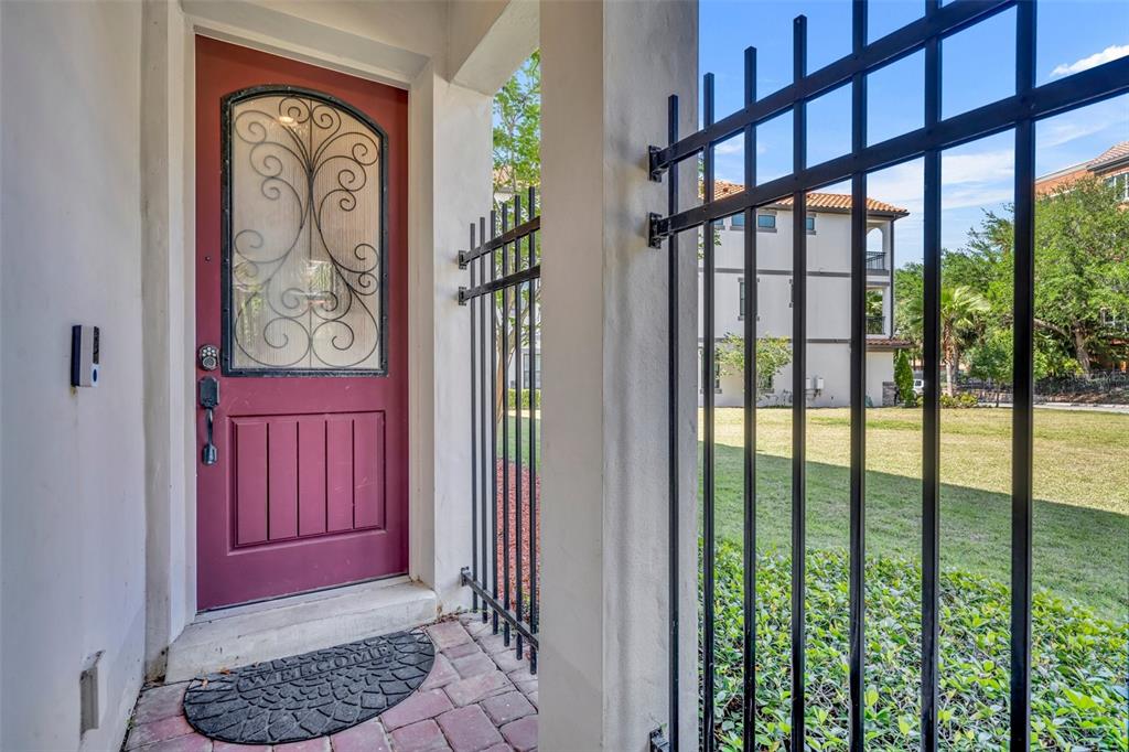 A red front door with a decorative glass insert sits behind a black metal gate — 7613 TOSCANA BOULEVARD, ORLANDO, FL