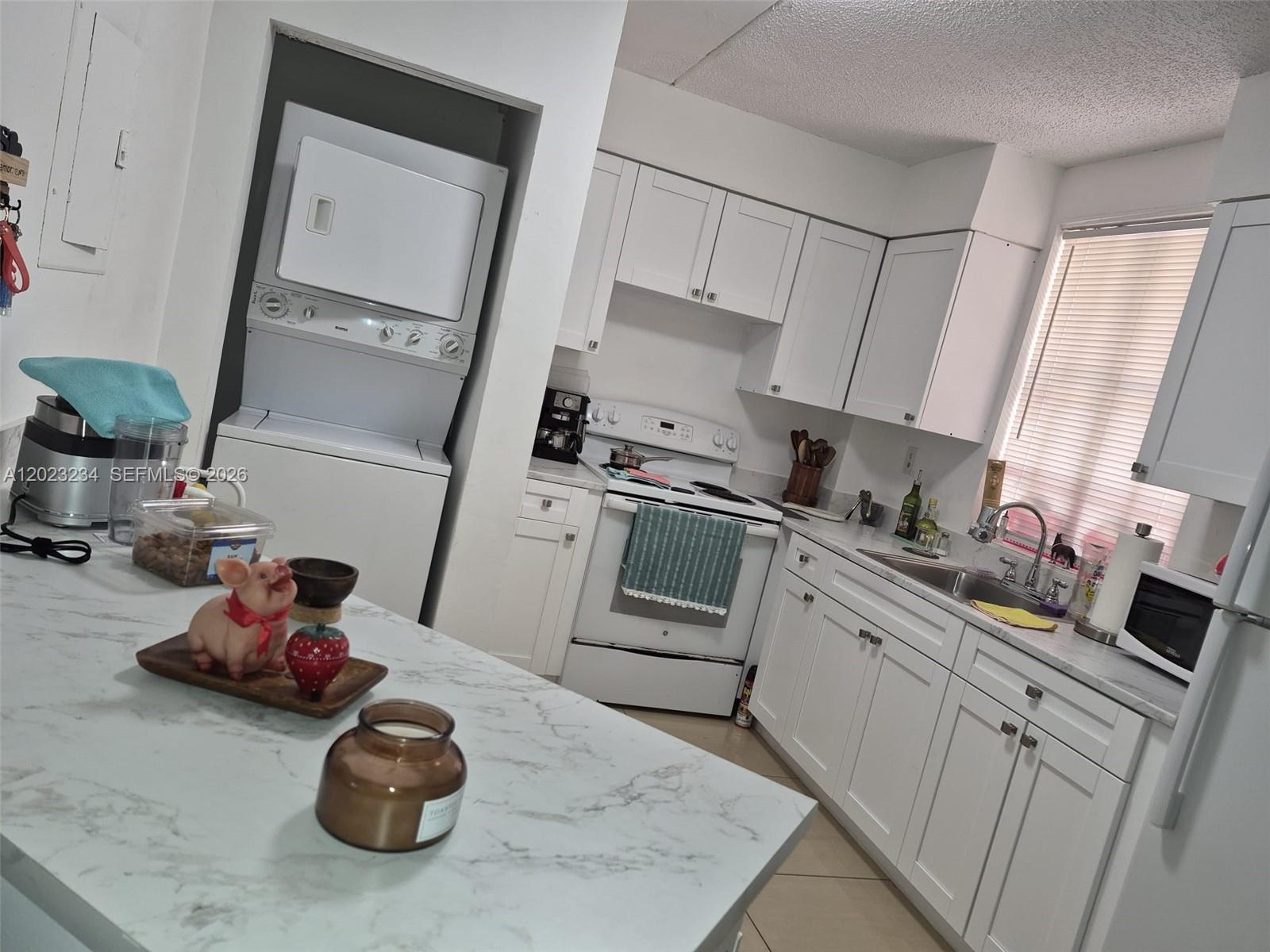 A kitchen features white cabinets, marble-look countertops, a stacked washer-dryer, and a central island — 6195 NW 186th St # 106, Hialeah FL 33015, HIALEAH, FL