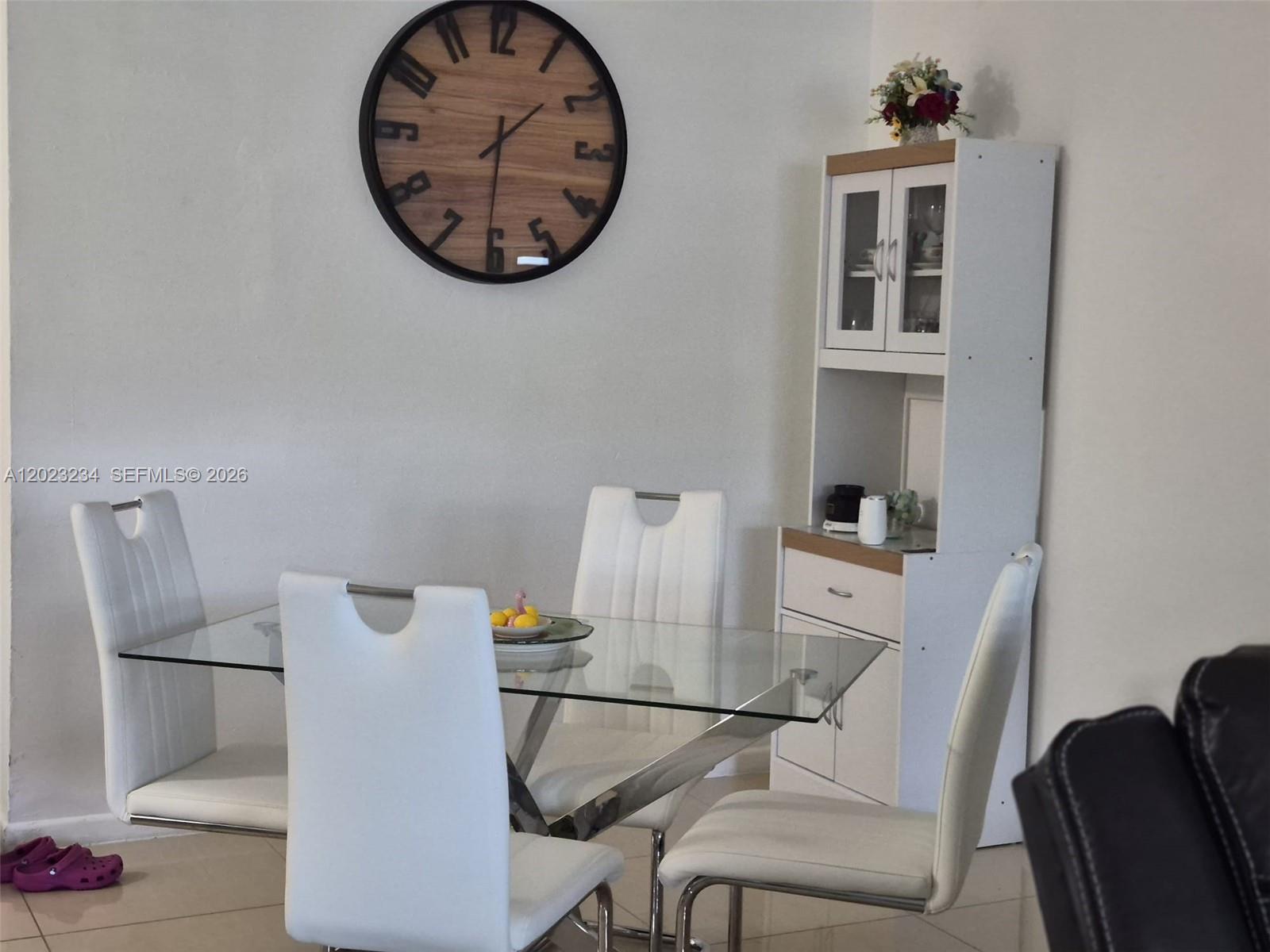 A dining area features a glass table, four white chairs, a wall clock, and a hutch — 6195 NW 186th St # 106, Hialeah FL 33015, HIALEAH, FL