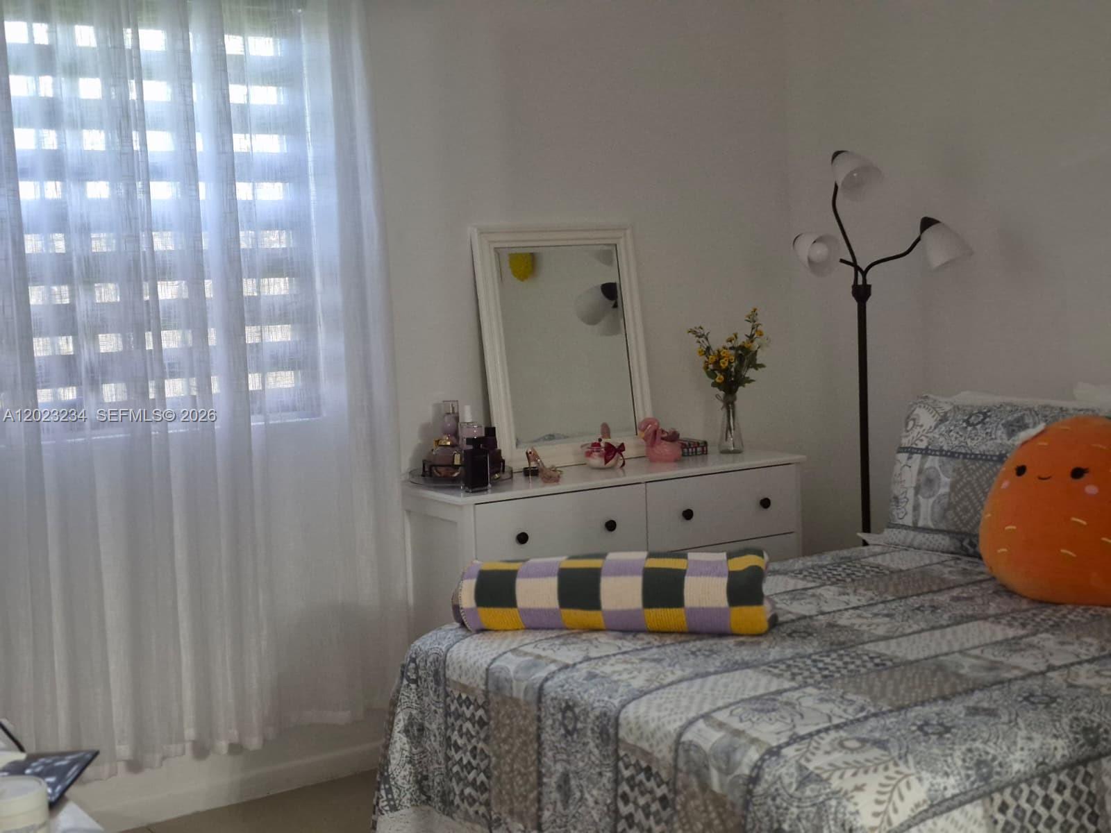 A bedroom features a white dresser with a mirror, a bed, and a floor lamp — 6195 NW 186th St # 106, Hialeah FL 33015, HIALEAH, FL