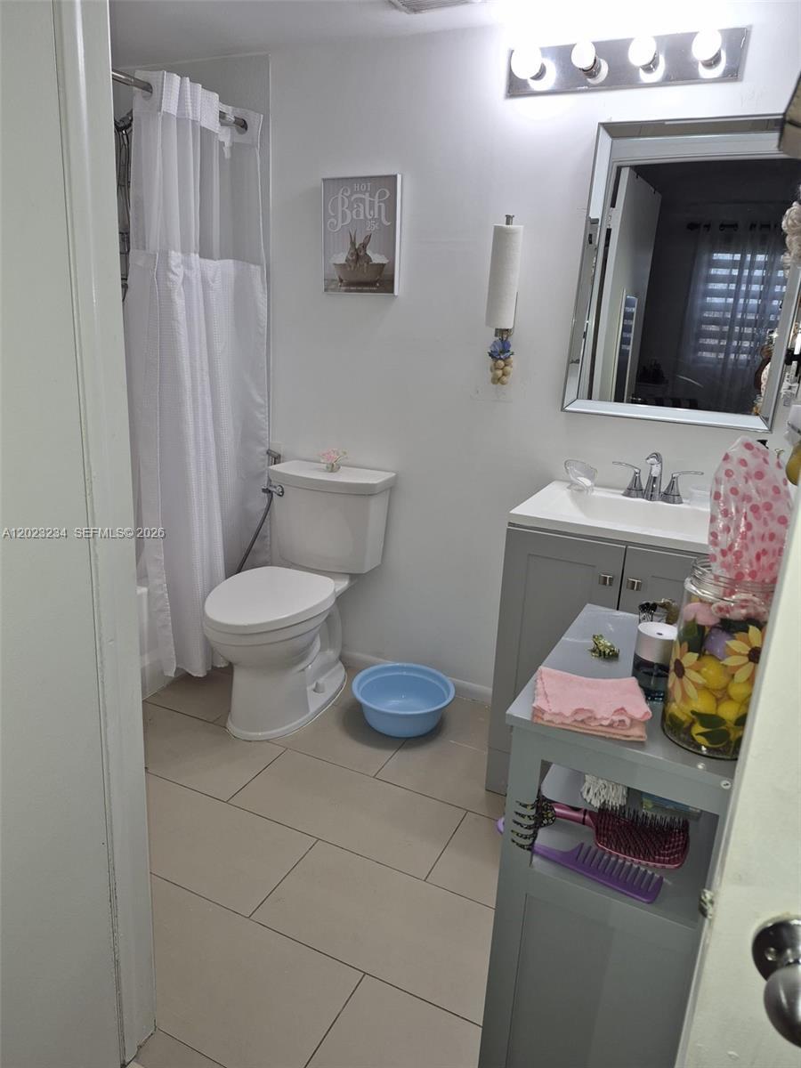 A bathroom features a white toilet, a gray vanity, a shower curtain, and tile flooring — 6195 NW 186th St # 106, Hialeah FL 33015, HIALEAH, FL