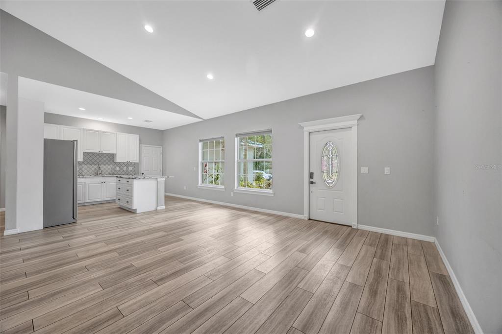 An open-concept living area features light wood-look flooring, gray walls, and an adjacent white kitchen — 2936 SE NORMAN AVENUE, ARCADIA, FL