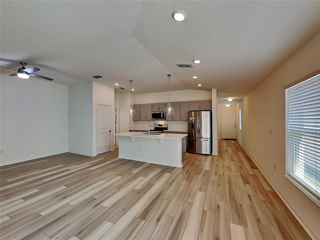 An open-concept kitchen and living area features light wood-look flooring, a central island, and stainless steel appliances — 1052 PAPAYA CIRCLE, DAVENPORT, FL