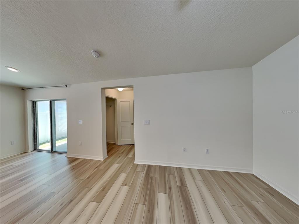An empty room features light wood-look flooring, white walls, and a sliding glass door — 1052 PAPAYA CIRCLE, DAVENPORT, FL