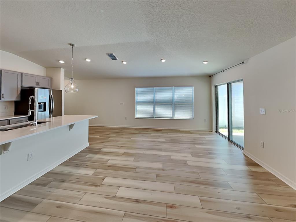 An open-concept kitchen and living area features light wood-look flooring and a sliding glass door — 1052 PAPAYA CIRCLE, DAVENPORT, FL