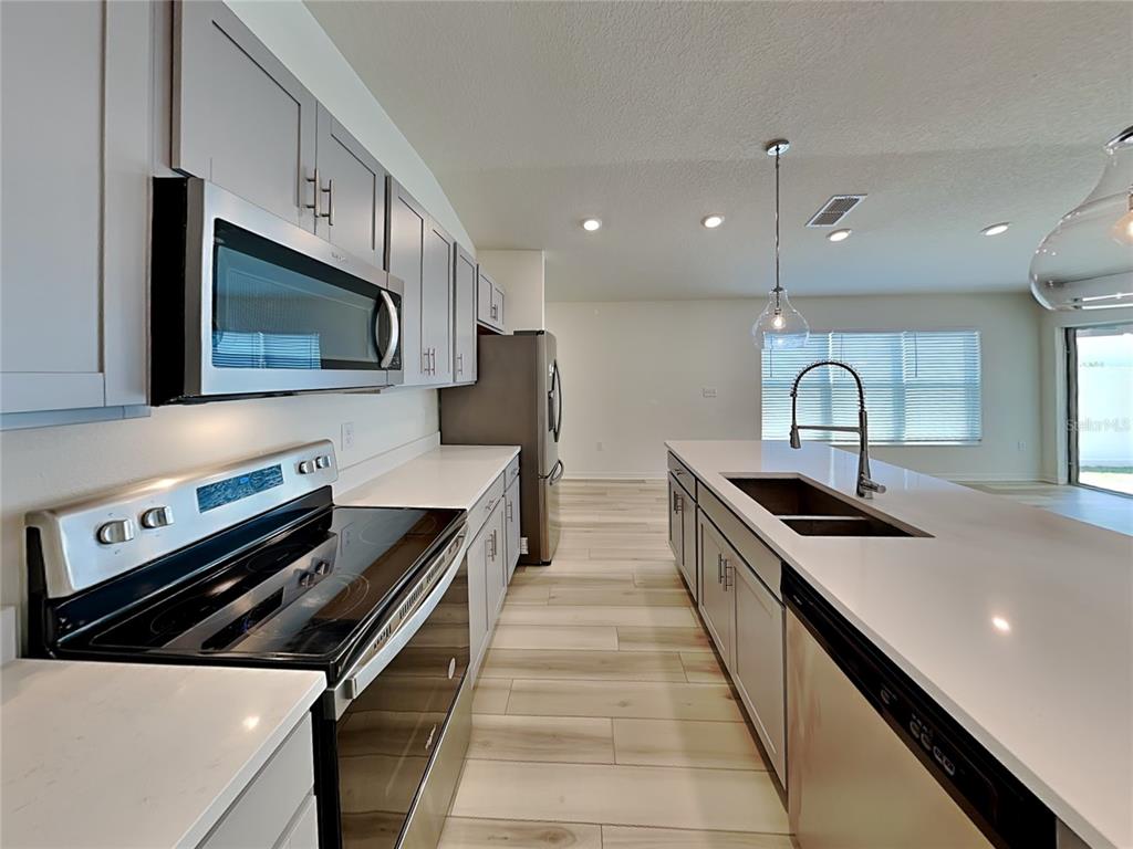 A modern kitchen features light gray cabinets, stainless steel appliances, and a large white island — 1052 PAPAYA CIRCLE, DAVENPORT, FL
