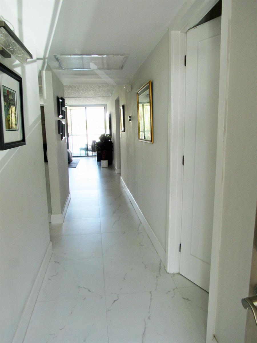 A hallway with white marble-look tile flooring leads toward a bright room with sliding doors — 21 Royal Palm Way # 2020, Boca Raton FL 33432, BOCA RATON, FL