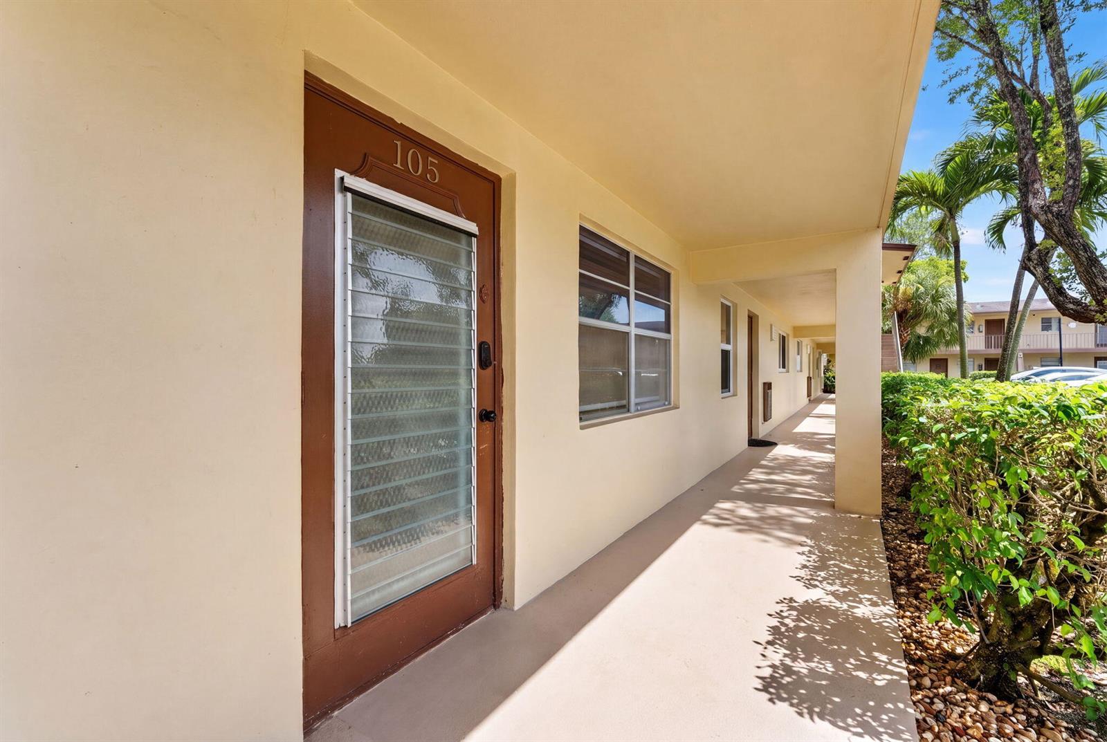 A brown door labeled 105 opens onto a covered outdoor walkway beside a hedge — 251 NW 76th Avenue # 105, Margate FL 33063, MARGATE, FL
