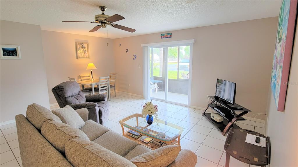 A living room with tile floors, a sofa, a dining set, and a sliding glass door — 2727 75TH ST W UNIT 7A2, BRADENTON, FL