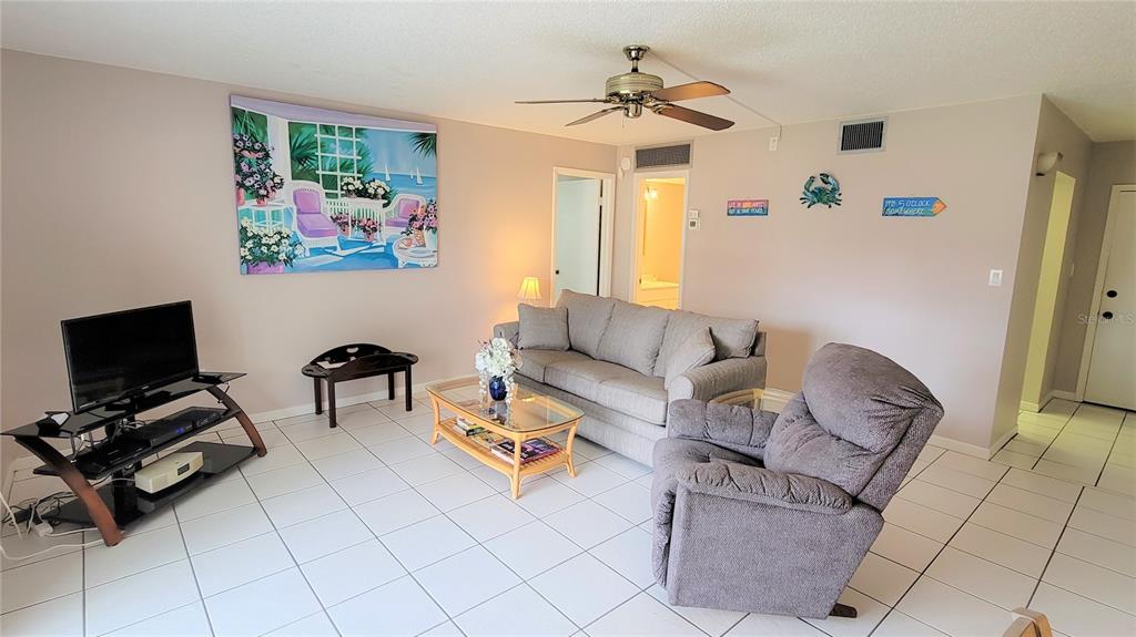 A living room features a gray sofa, a recliner, a glass coffee table, and tile flooring — 2727 75TH ST W UNIT 7A2, BRADENTON, FL