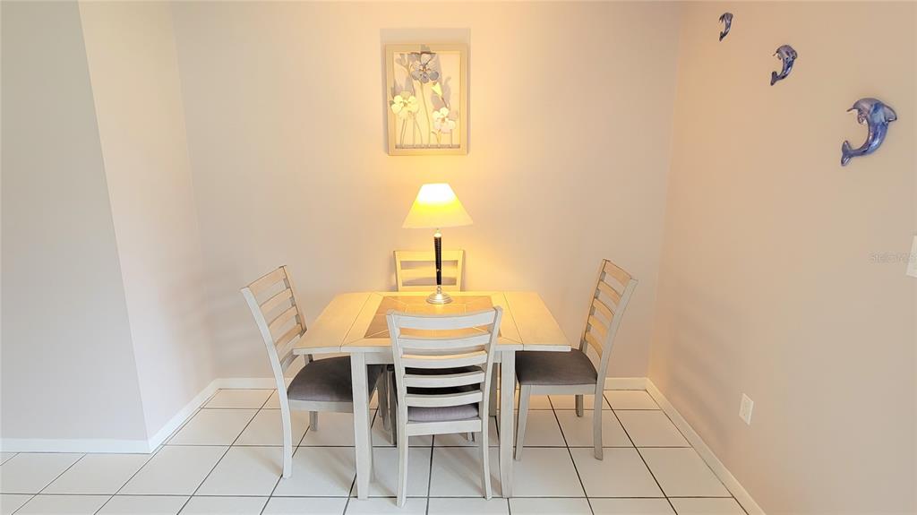 A dining area features a square table with four chairs, a lamp, and wall art — 2727 75TH ST W UNIT 7A2, BRADENTON, FL