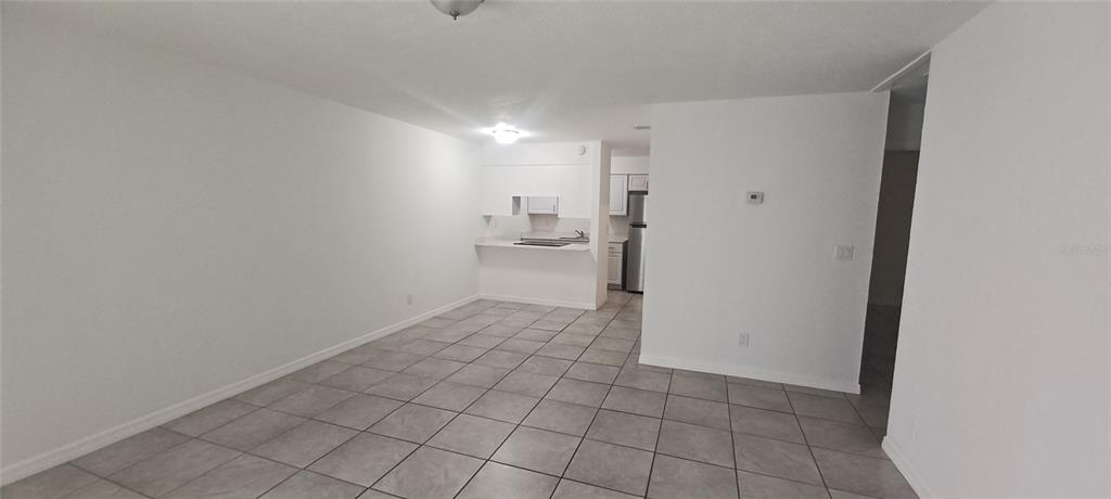An open-concept living area with white walls and light-colored tile flooring leads to a kitchen — 5200 SE 31ST STREET SE UNIT D, OCALA, FL