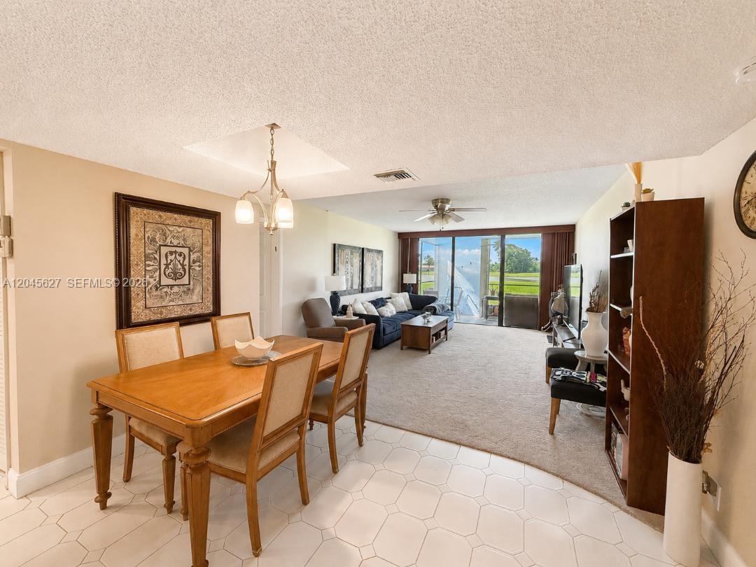 A dining area with a wooden table transitions into a carpeted living room with balcony access — 16325 Golf Club Rd # 111, Weston FL 33326, WESTON, FL