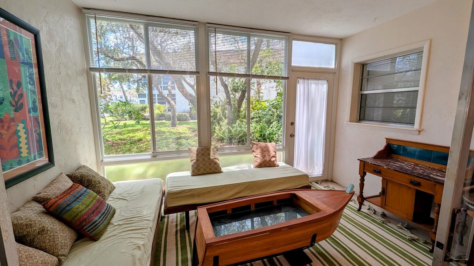 A sunroom features two daybeds, a boat-shaped coffee table, and large windows overlooking greenery — 2950 SE Ocean Boulevard # 2, Stuart FL 34996, STUART, FL