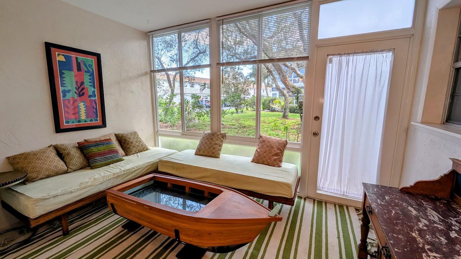 A sunroom features two daybeds, a boat-shaped coffee table, and large windows overlooking a lawn — 2950 SE Ocean Boulevard # 2, Stuart FL 34996, STUART, FL