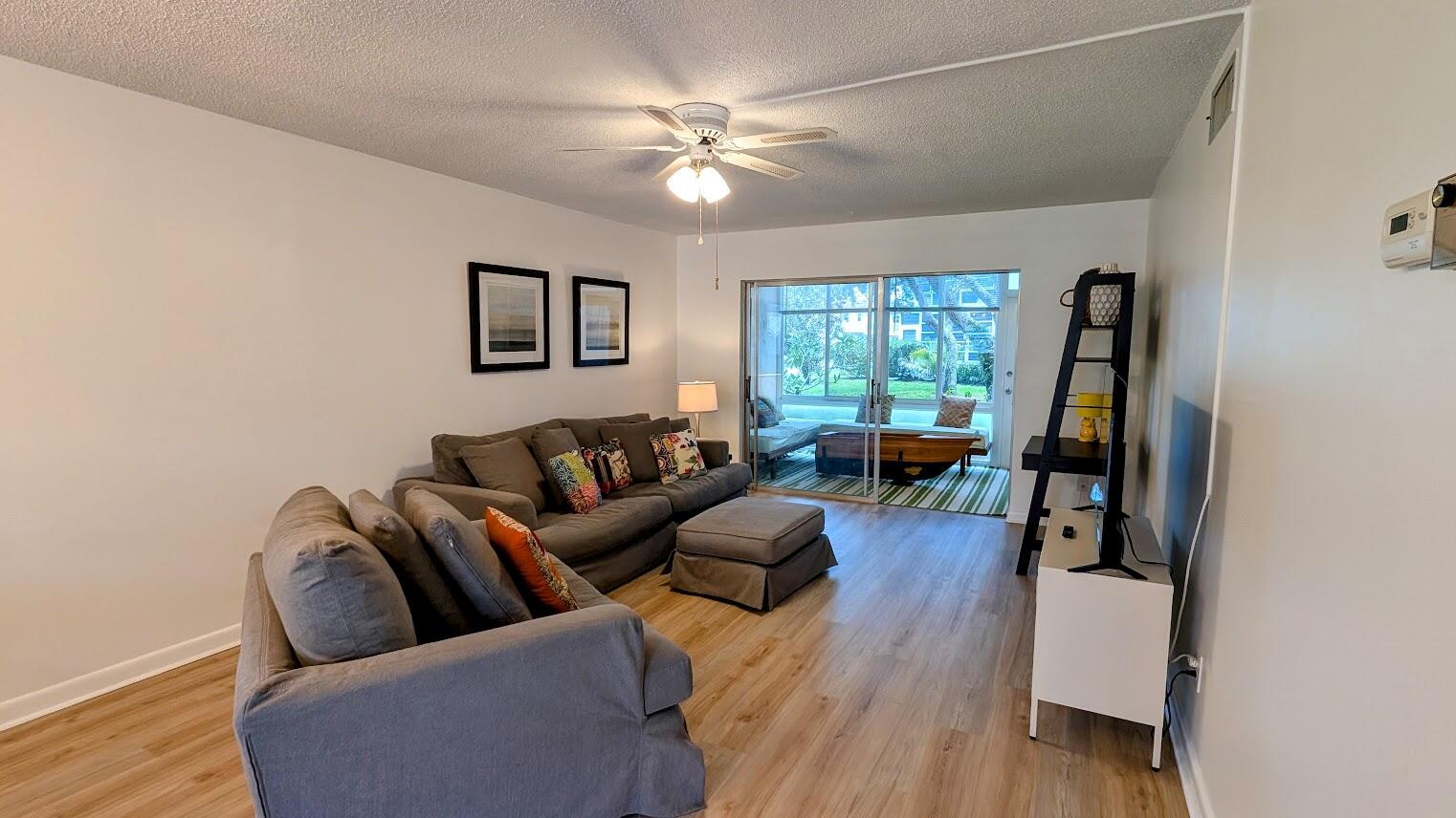 A living room with light wood floors, a grey sectional sofa, and a sliding glass door — 2950 SE Ocean Boulevard # 2, Stuart FL 34996, STUART, FL