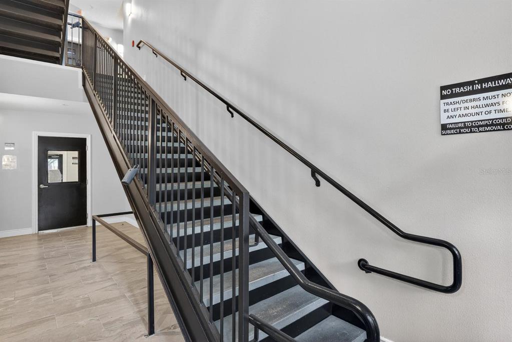 A metal staircase with a handrail ascends along a white wall in a building hallway — 1185 SW 9TH ROAD UNIT 212, GAINESVILLE, FL
