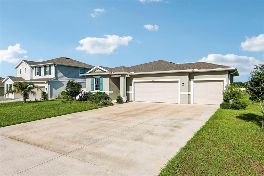 A single-story house with a three-car garage and a concrete driveway under a blue sky — 31719 BROADWATER AVENUE, LEESBURG, FL