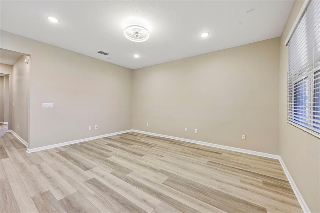 An empty room with light wood-look flooring, beige walls, recessed lighting, and a window — 31719 BROADWATER AVENUE, LEESBURG, FL
