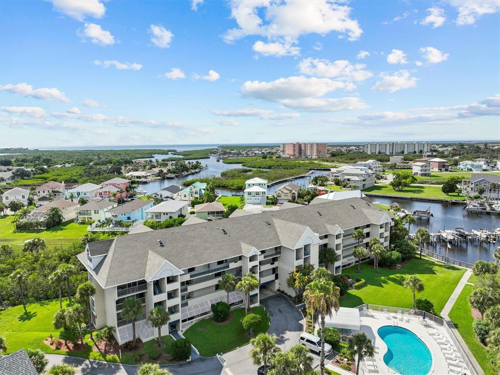 An aerial view shows a multi-story apartment building with a swimming pool and nearby waterways — 5537 SEA FOREST DRIVE UNIT 307, NEW PORT RICHEY, FL