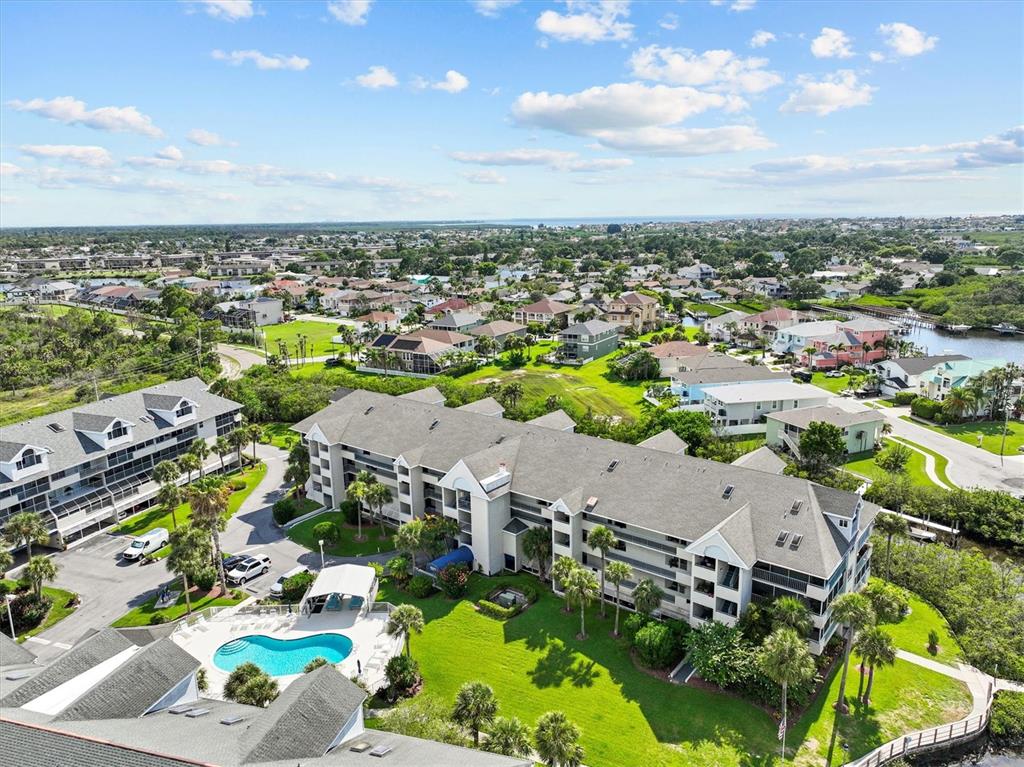 An aerial view shows a multi-story apartment building with a swimming pool and surrounding neighborhood — 5537 SEA FOREST DRIVE UNIT 307, NEW PORT RICHEY, FL