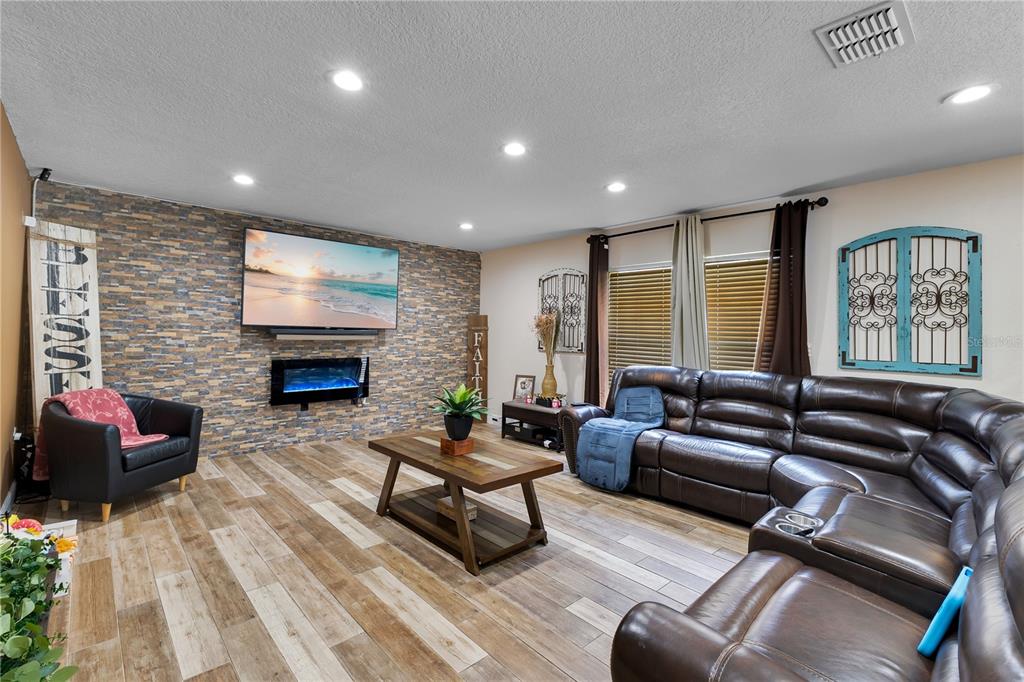 A living room features a stone accent wall with a fireplace, television, and leather sectional — 5051 PLYMOUTH TURTLE CIRCLE, ST CLOUD, FL