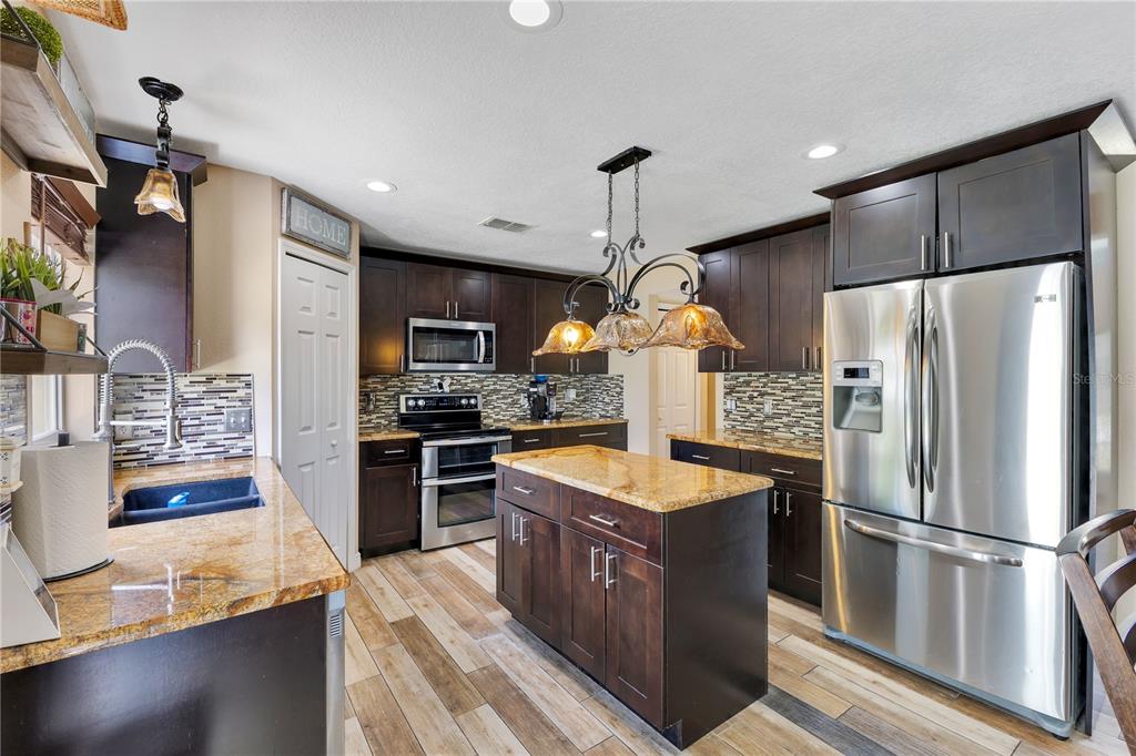 A kitchen features dark wood cabinetry, granite countertops, stainless steel appliances, and a central island — 5051 PLYMOUTH TURTLE CIRCLE, ST CLOUD, FL