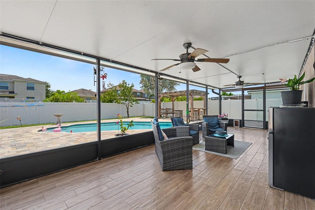 A covered patio features wood-look tile flooring, wicker furniture, and a view of a swimming pool — 11531 MISTY ISLE LANE, RIVERVIEW, FL