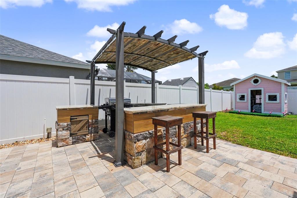 An outdoor kitchen with a stone base, granite countertop, and pergola sits on a patio — 11531 MISTY ISLE LANE, RIVERVIEW, FL