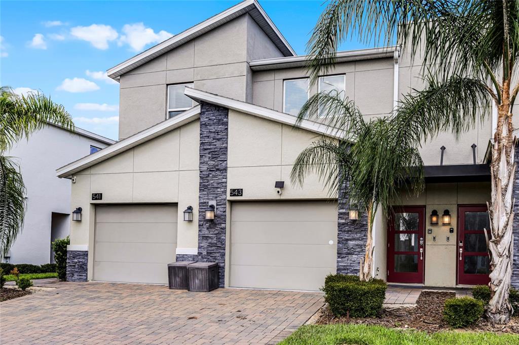 A two-story townhouse exterior features a stone-accented facade, two garage doors, and red entry doors — 543 OCEAN COURSE AVENUE, DAVENPORT, FL