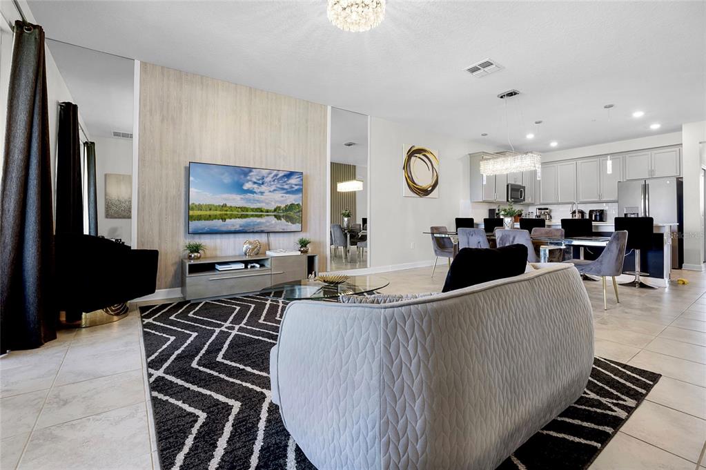 A modern open-concept living and dining area with a light wood accent wall and tile flooring — 543 OCEAN COURSE AVENUE, DAVENPORT, FL