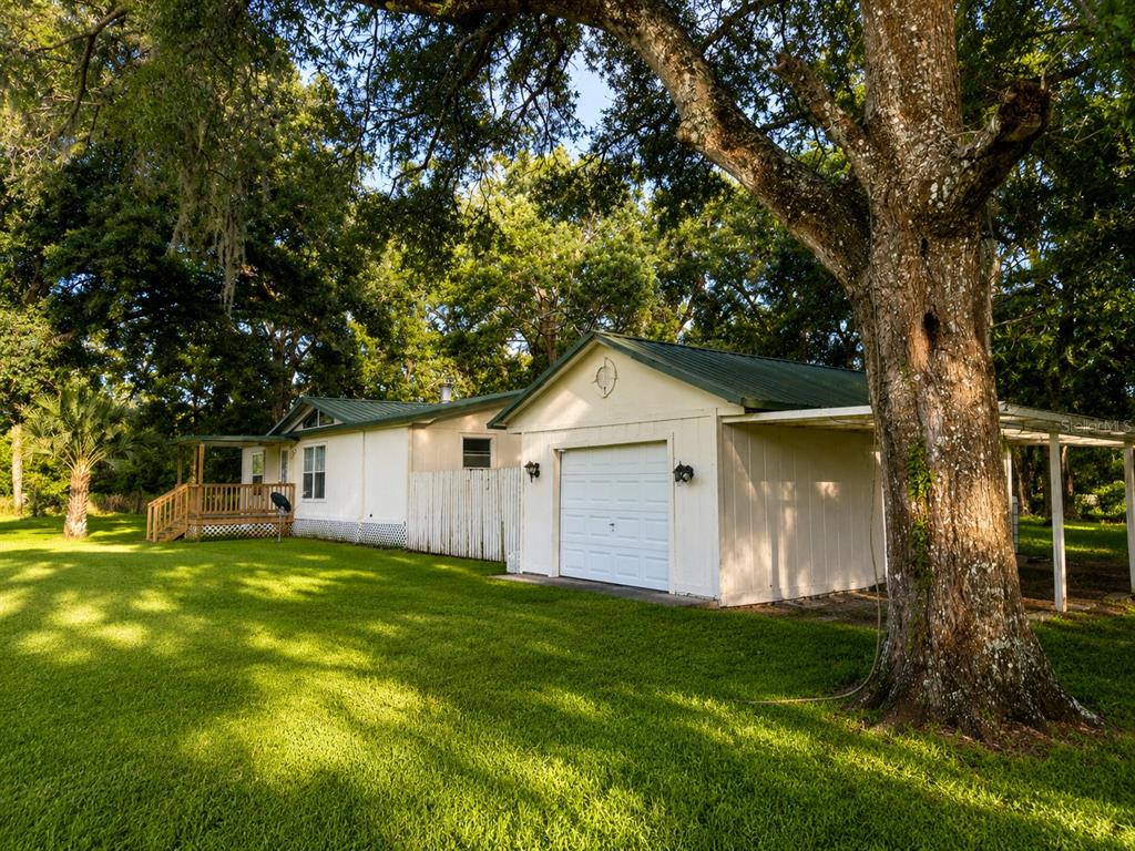 A light-colored house with a metal roof, attached garage, and wooden porch sits on grass — 25256 RICHBARN ROAD, BROOKSVILLE, FL