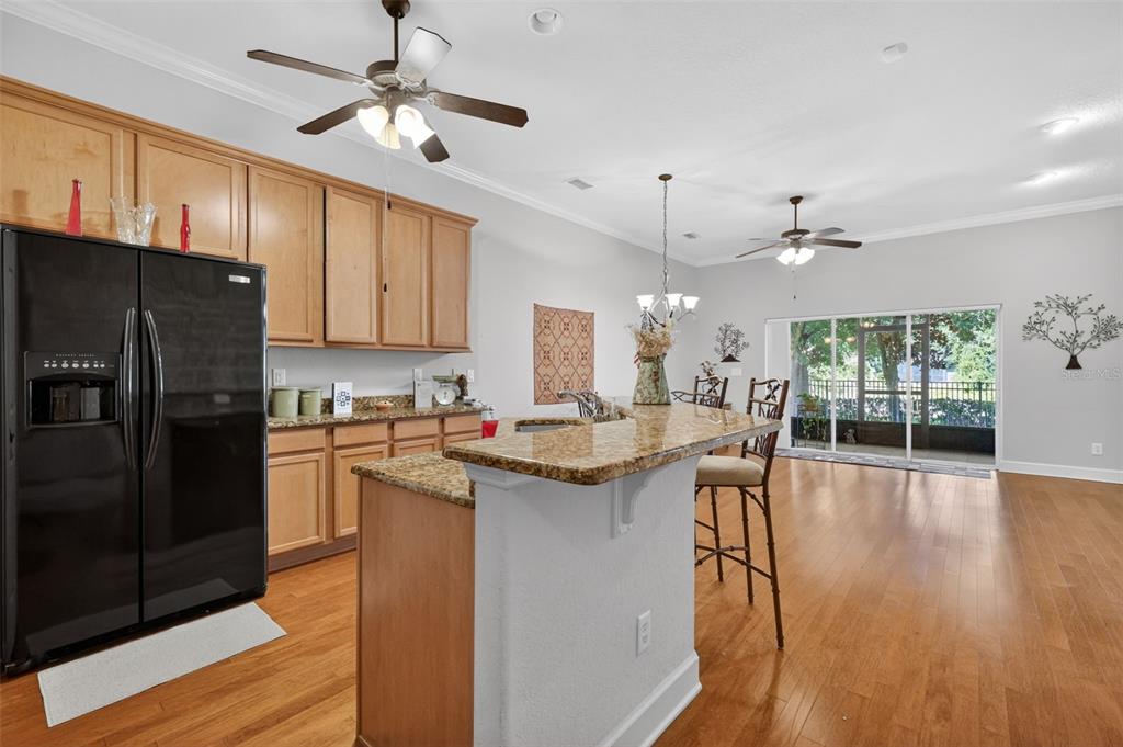 A kitchen with wood cabinets, granite countertops, and a breakfast bar opens to a dining area — 1010 GREEN GATE BOULEVARD, GROVELAND, FL