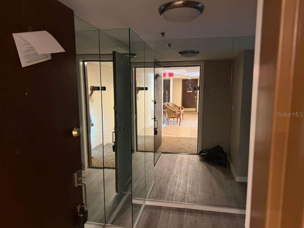 An entryway features mirrored walls, light wood-look flooring, and a view into a hallway — 7432 SUNSHINE SKYWAY LANE S UNIT 206, ST PETERSBURG, FL