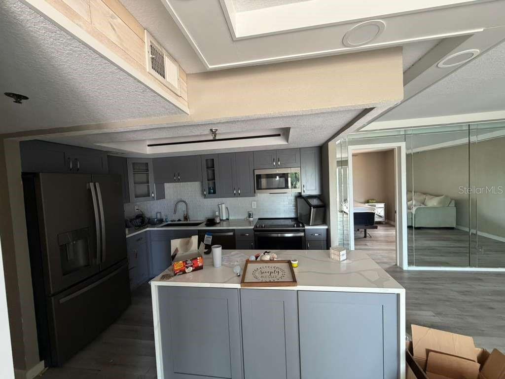 A kitchen features gray cabinets, a white quartz island, and stainless steel appliances — 7432 SUNSHINE SKYWAY LANE S UNIT 206, ST PETERSBURG, FL
