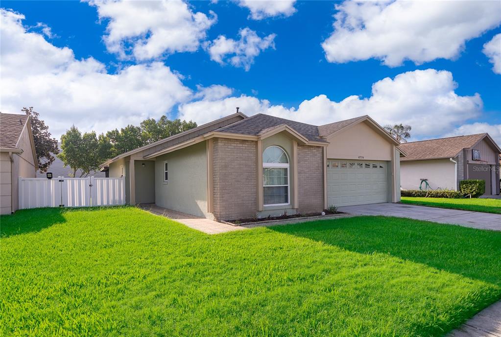 A single-story house with a tan stucco and brick exterior, a garage, and a lawn — 4779 WARRIOR LANE, KISSIMMEE, FL