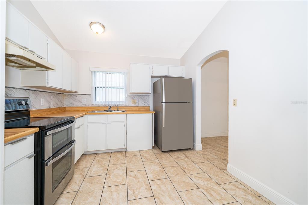 A kitchen features white cabinets, stainless steel appliances, wood-look countertops, and light-colored tile flooring — 4779 WARRIOR LANE, KISSIMMEE, FL