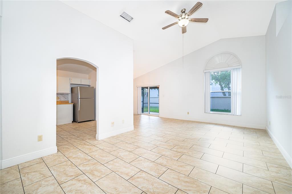 A bright living room with vaulted ceilings, tile flooring, and an arched entryway to the kitchen — 4779 WARRIOR LANE, KISSIMMEE, FL