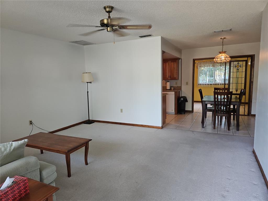 A living room with carpeted floors leads to a dining area with a tile floor — 11087 SW 77TH COURT, OCALA, FL