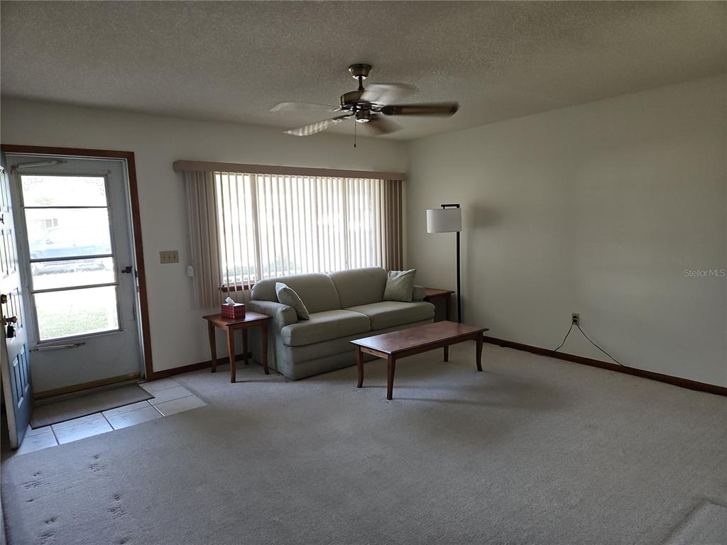 A living room features beige carpeting, a light green sofa, a coffee table, and vertical blinds — 11087 SW 77TH COURT, OCALA, FL