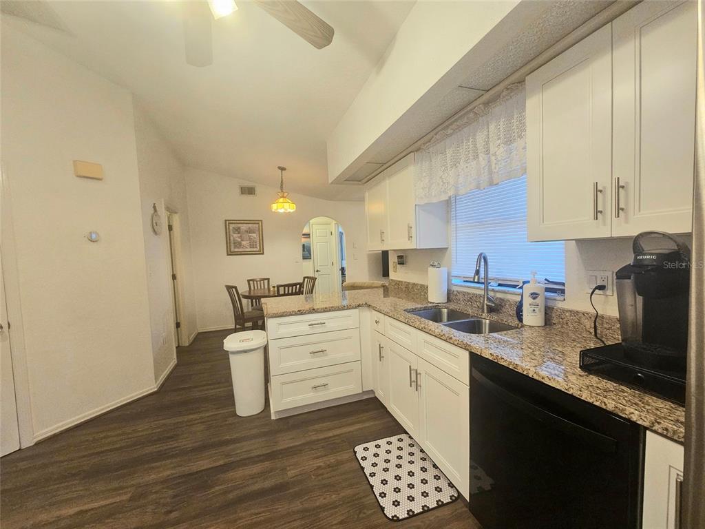 A kitchen with white cabinets, granite countertops, and dark wood-look flooring opens to a dining area — 1011 TROPICAL AVENUE NW, PORT CHARLOTTE, FL