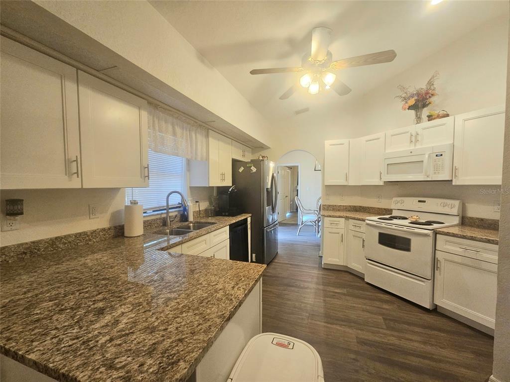 A kitchen features white cabinets, granite countertops, white appliances, and wood-look flooring — 1011 TROPICAL AVENUE NW, PORT CHARLOTTE, FL