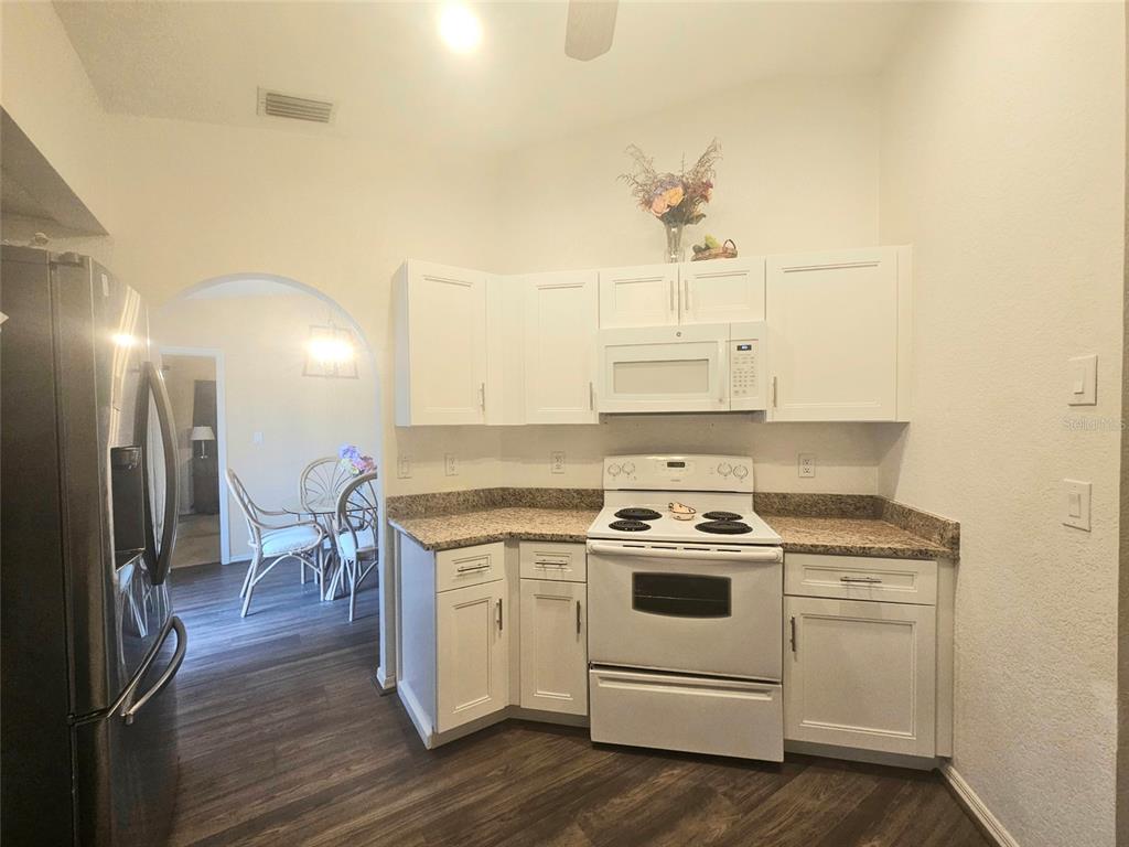 A kitchen features white cabinets, granite countertops, a white stove, and a black refrigerator — 1011 TROPICAL AVENUE NW, PORT CHARLOTTE, FL
